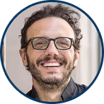 Homme souriant portant des lunettes avec des cheveux bouclés et une barbe légère.