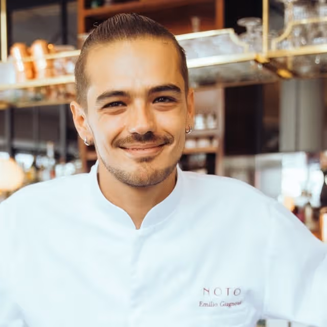 Jeune homme souriant portant une veste de chef blanc dans un restaurant.