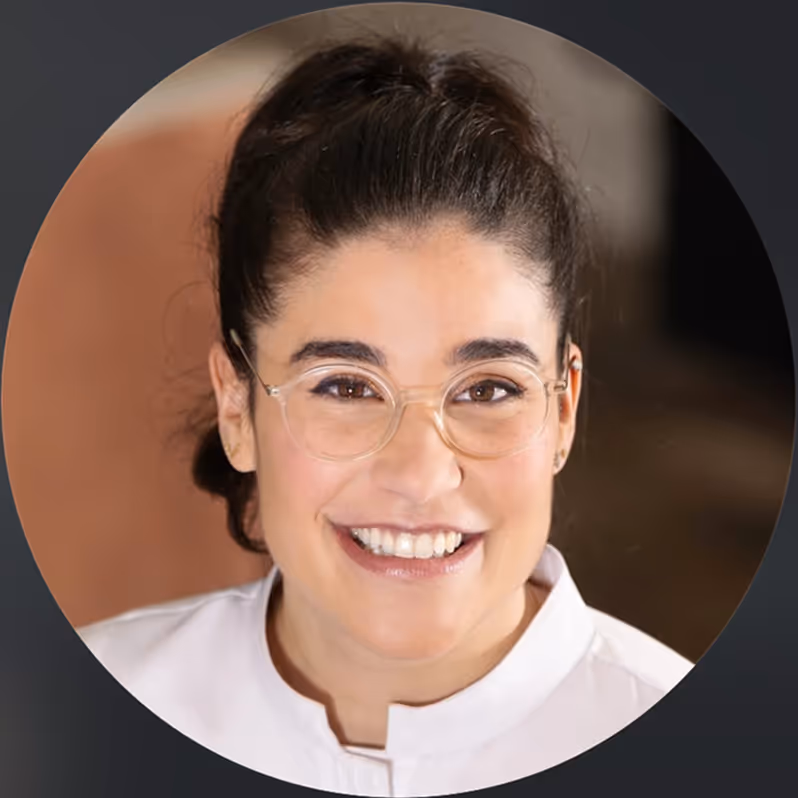 Portrait d'une femme souriante portant des lunettes transparentes et une blouse blanche, cheveux attachés.
