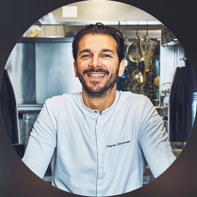 Homme souriant en veste de chef blanc dans une cuisine professionnelle.