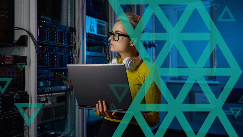 Woman wearing glasses and headphones holding a laptop in a server room with network equipment racks.