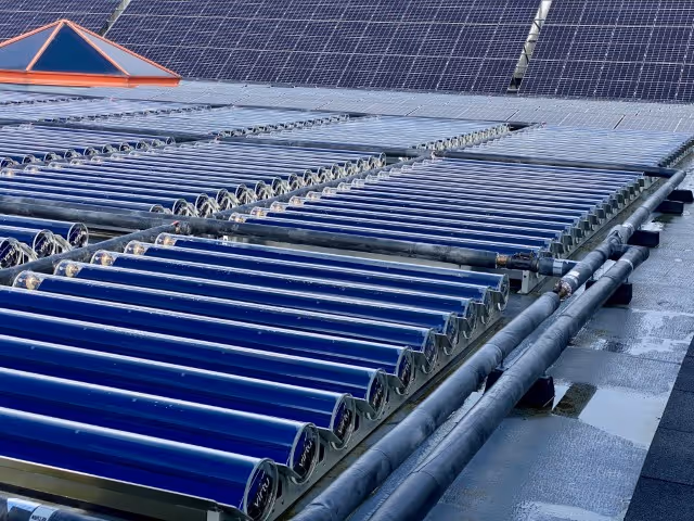 Solar thermal collectors on flat commercial roof and solar pv panels in background.