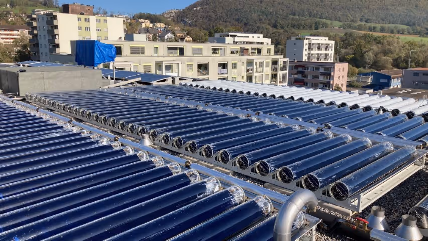 Solar thermal collectors on flat roof with residential buildings in the background.