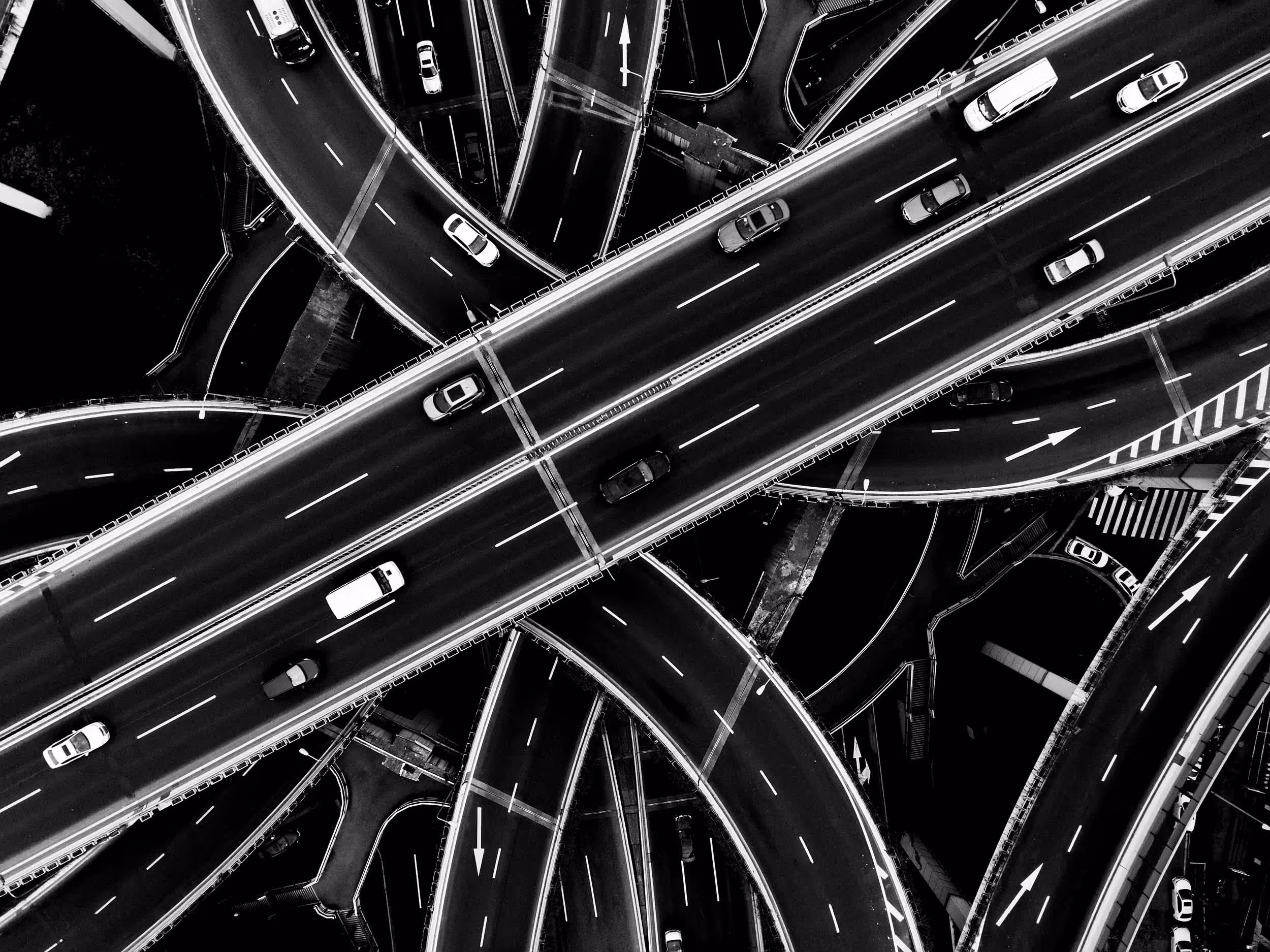 Aerial black and white view of a multi-level highway interchange with cars moving in different directions.