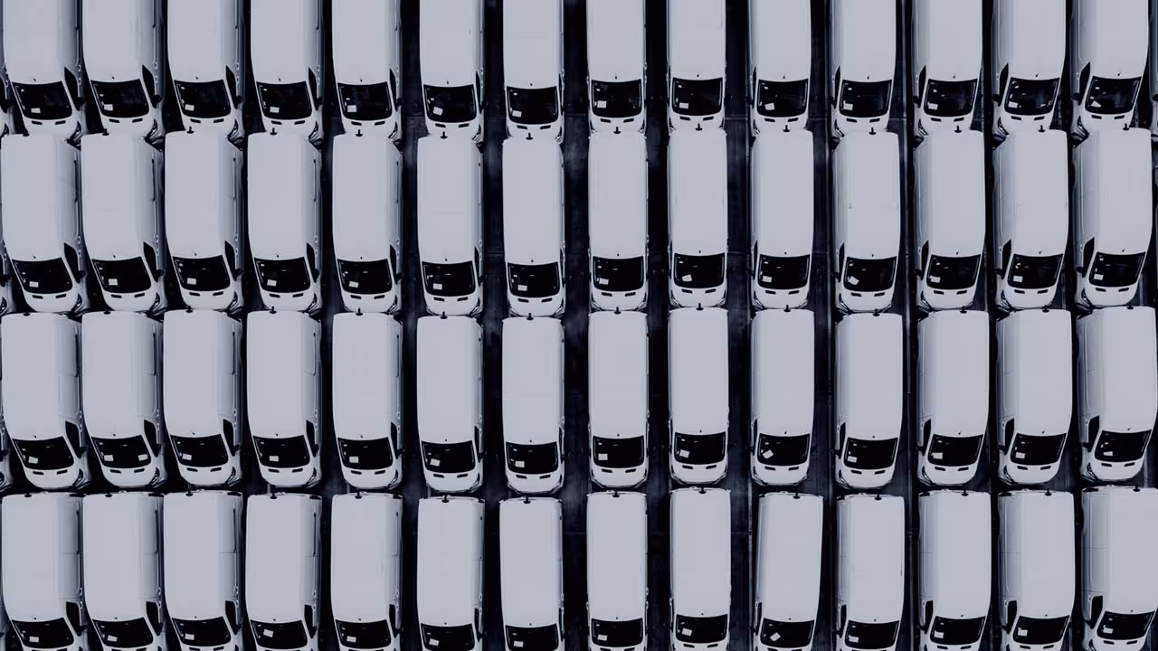 Aerial view of multiple white vans parked in neat, parallel rows on a dark surface.