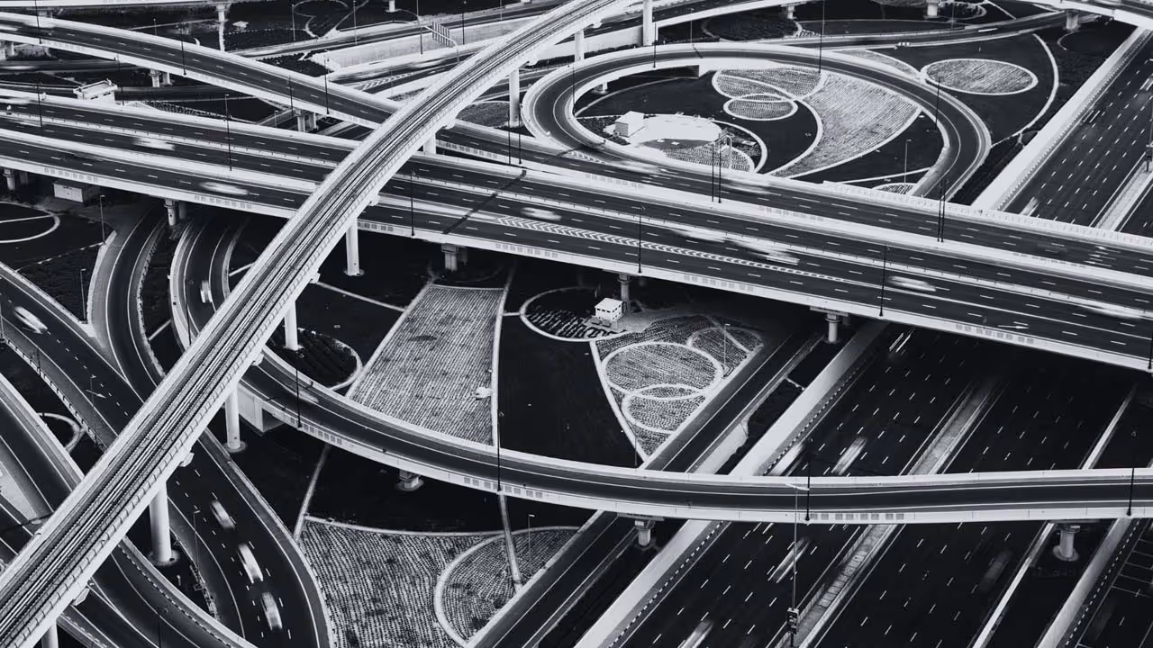 Black and white aerial view of a complex highway interchange with multiple overpasses and curved ramps.