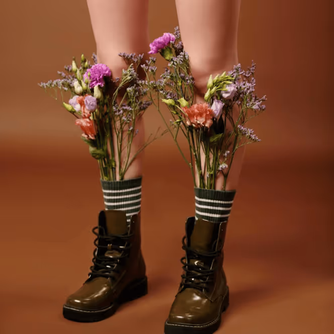 Legs wearing green boots with striped socks, filled with colorful flowers inside the boots.