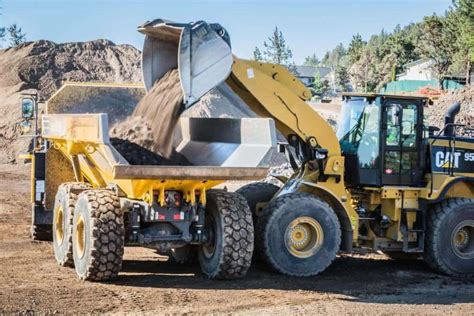Yellow front loader unloading dirt into a large dump truck at a construction site.