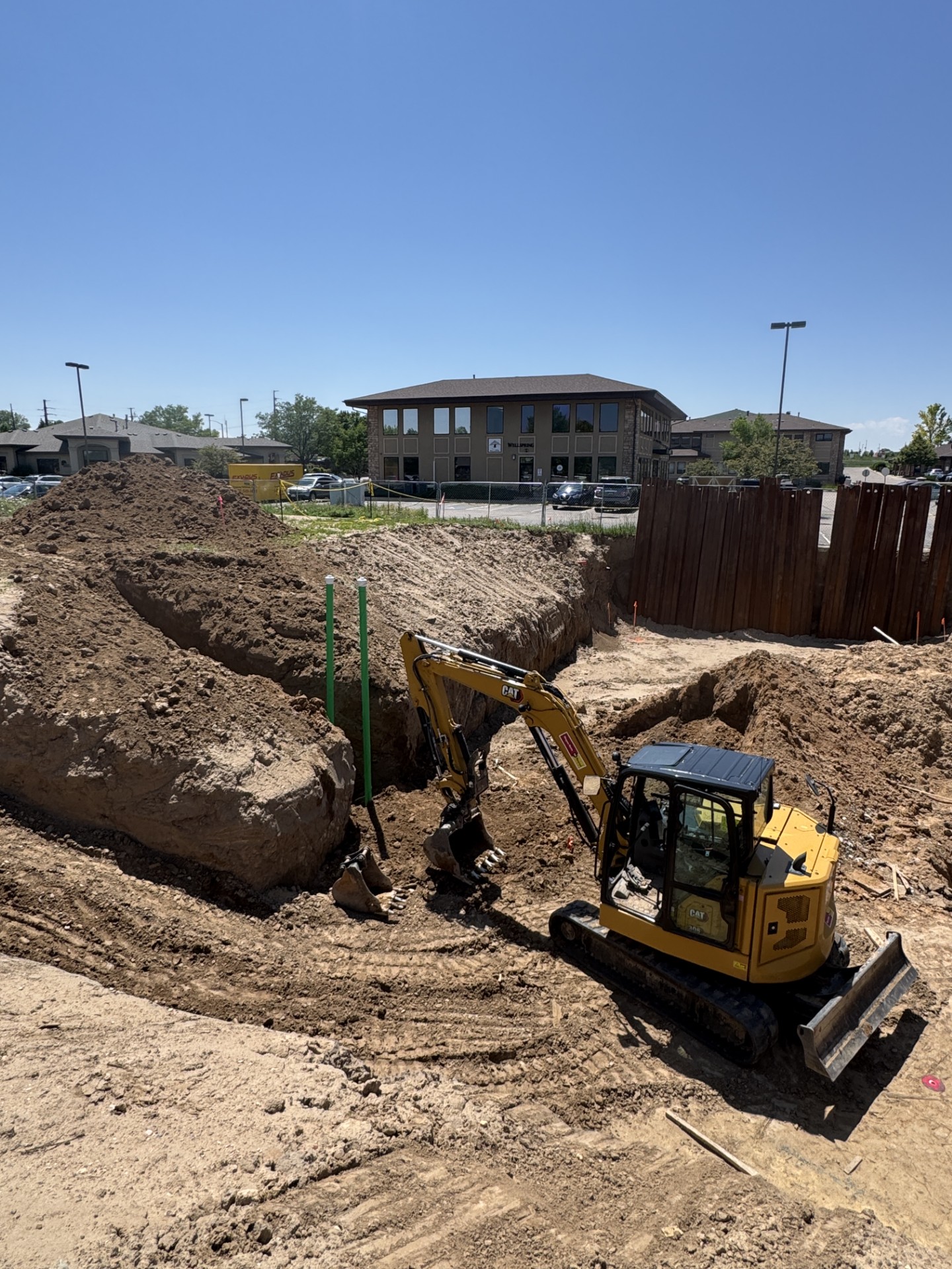 Yellow excavator digging a large hole at a construction site under clear blue sky.