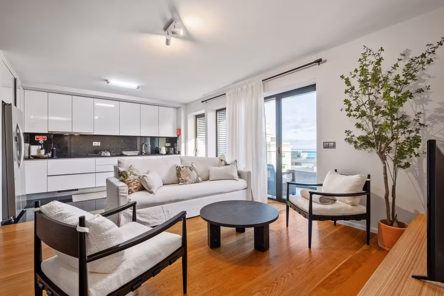Bright modern living room with white sofa, open kitchen, and balcony view at an Island Escape apartment in Madeira.