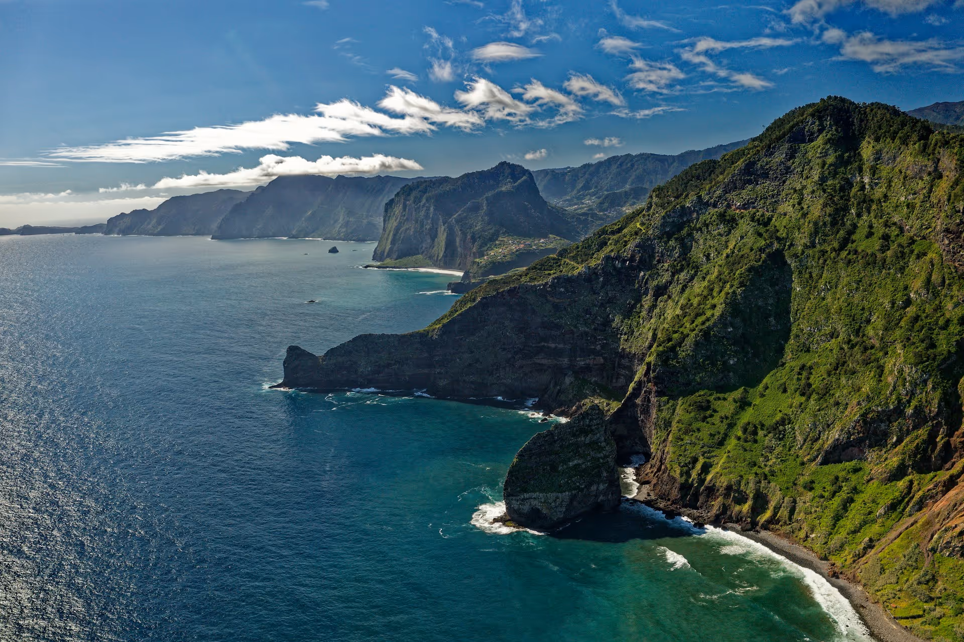 Aerial view of Madeira’s dramatic green cliffs and deep blue Atlantic Ocean on a sunny day.