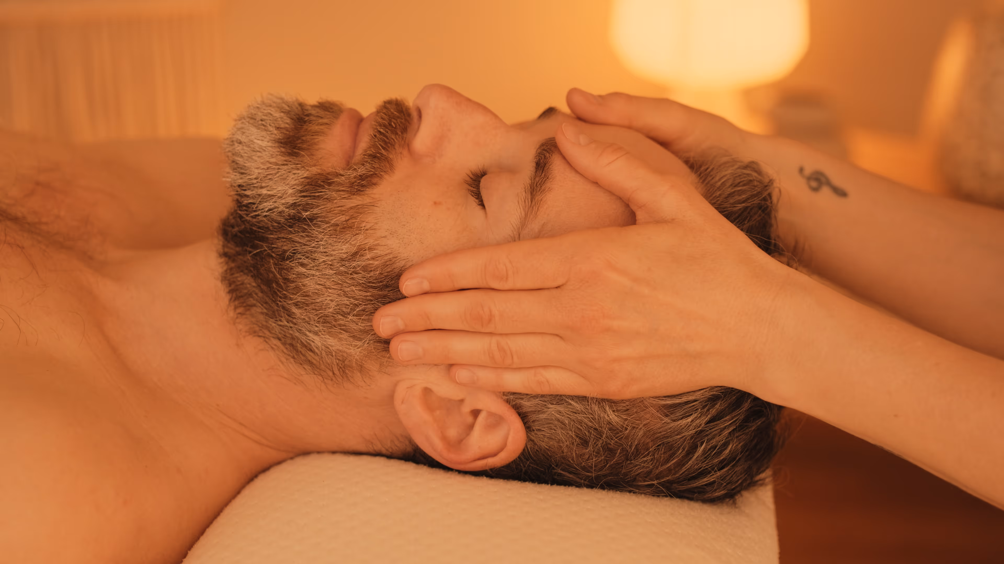 Ein Mann erhält eine Kopfmassage in warm beleuchtetem Raum.