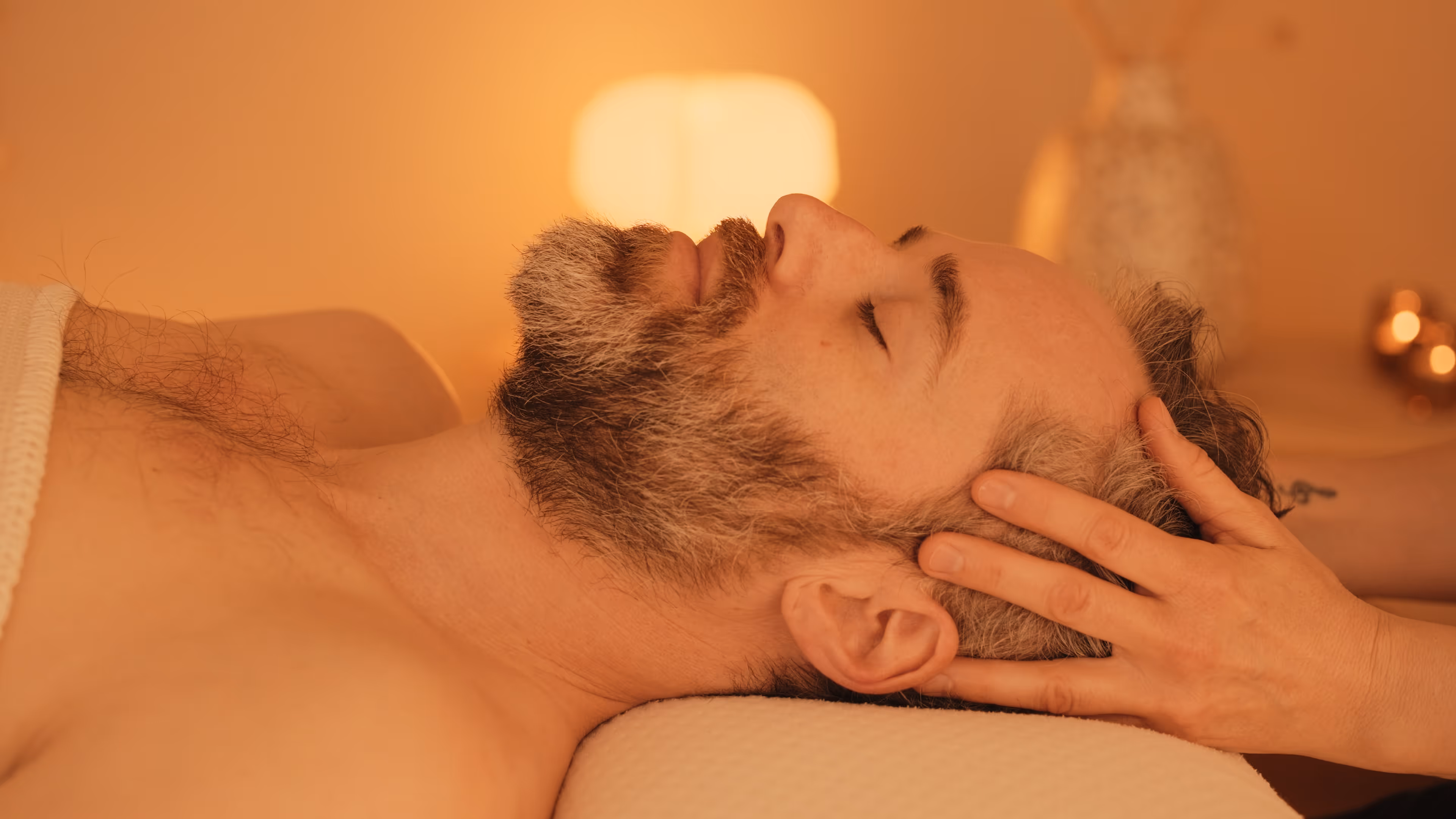 Ein Mann erhält eine Kopfmassage in warm beleuchtetem Raum.