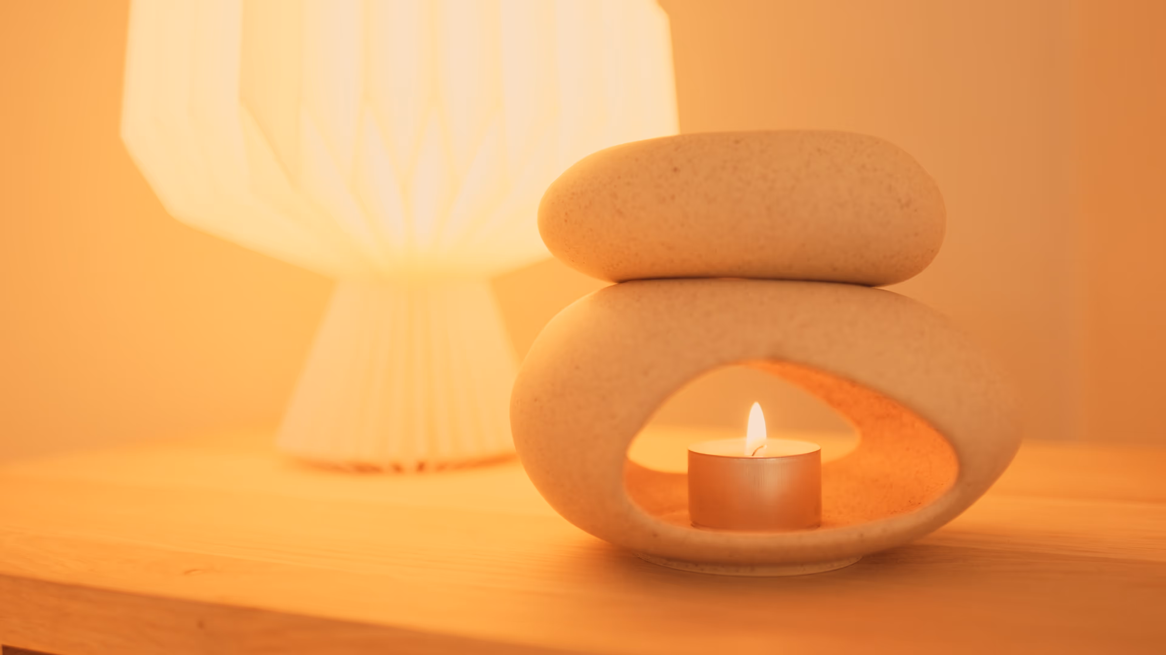 Teelicht in einem dekorativen Steinhalter auf einem Holztisch mit einer warm leuchtenden Lampe im Hintergrund.