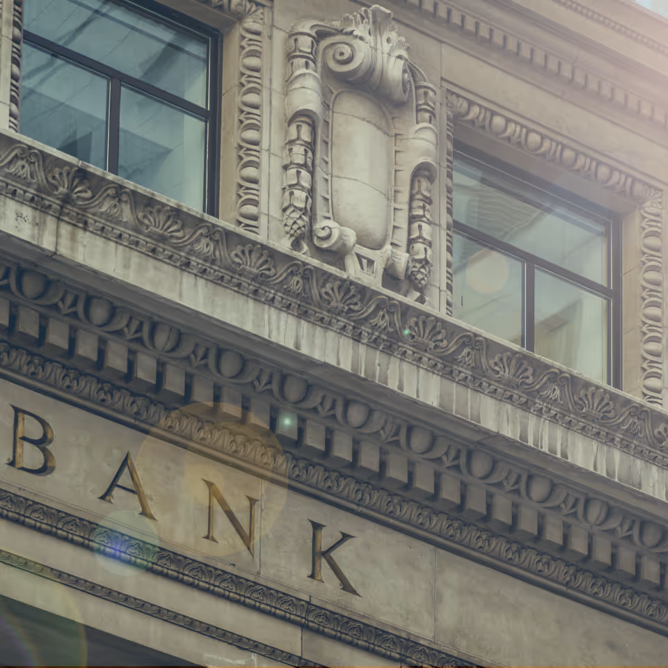Close-up of ornate stone facade with gold lettering spelling 'BANK' and two windows above.