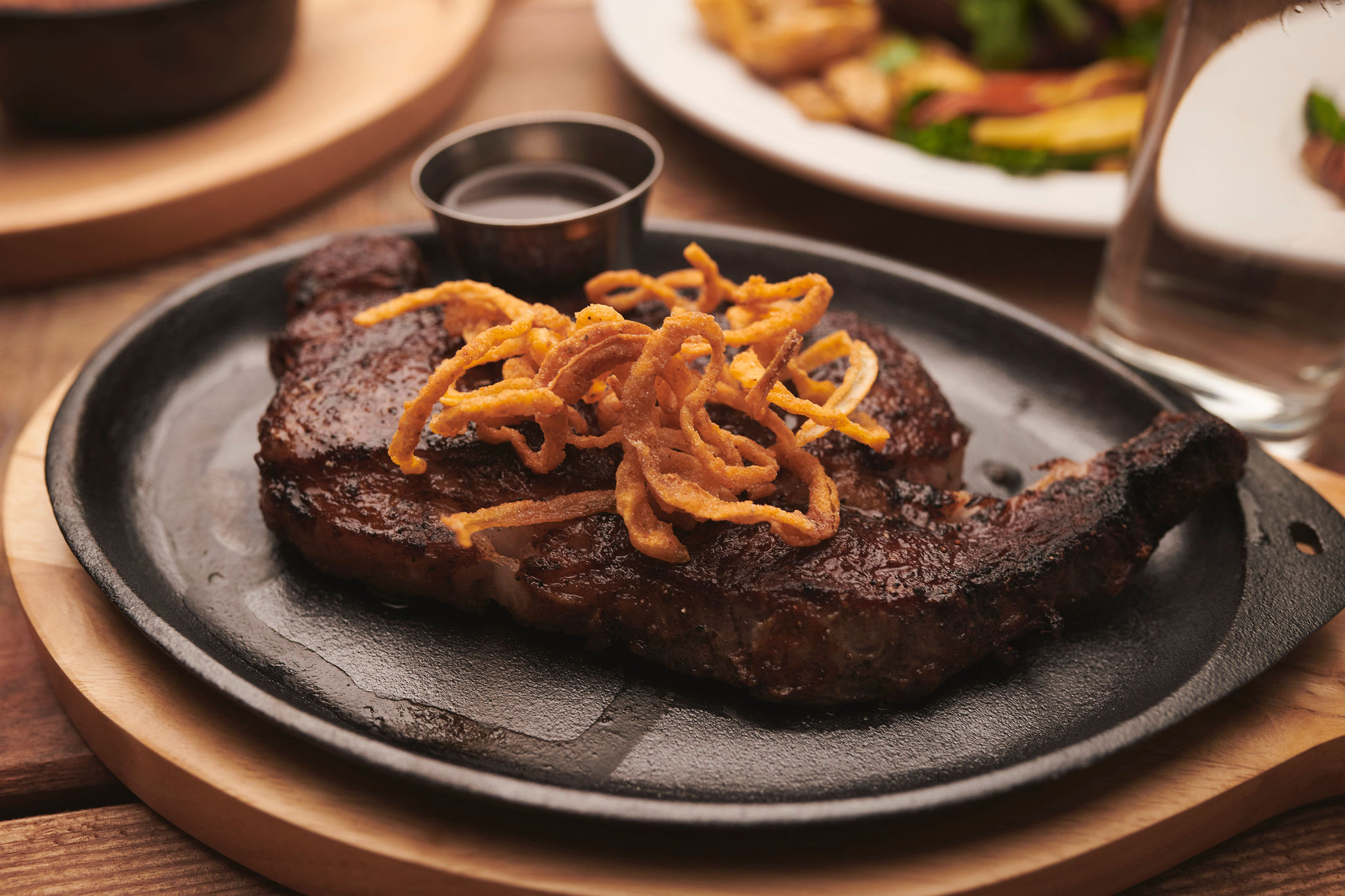 A ribeye steak with crispy onions on a cast iron dish.
