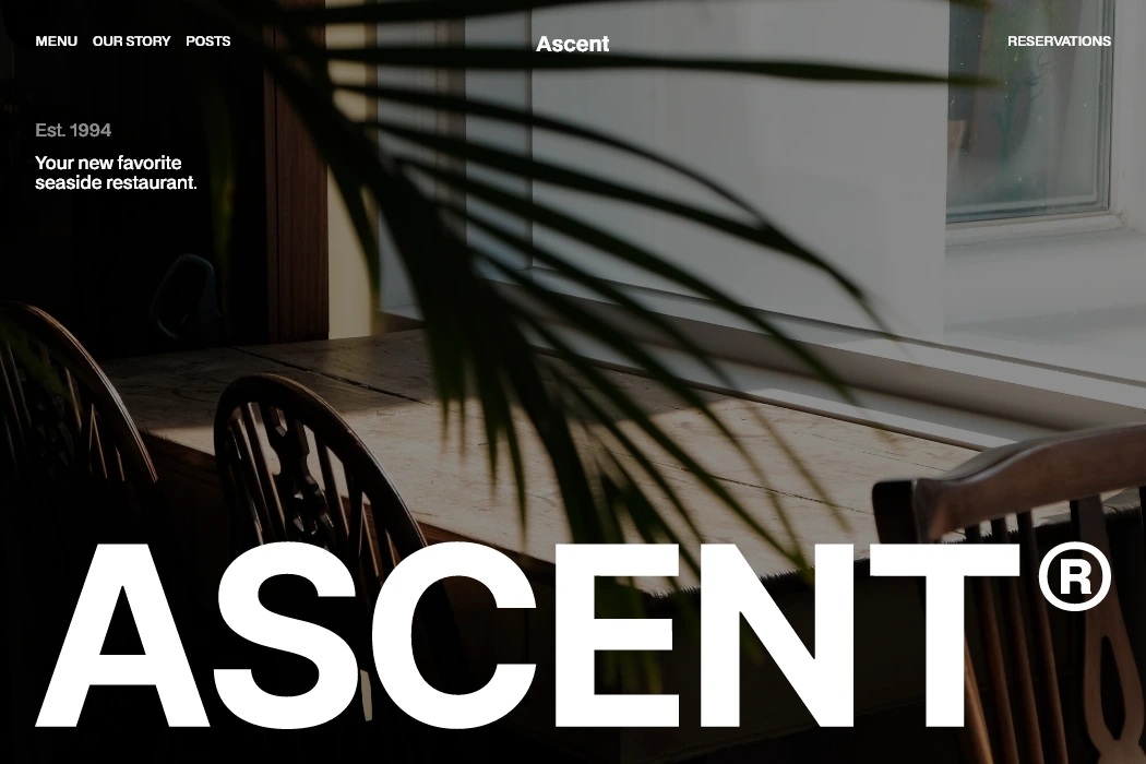 Vue d'une table en bois clair avec chaises autour, décorée par l'ombre d'une plante, texte blanc indiquant ASCENT®, restaurant en bord de mer depuis 1994.