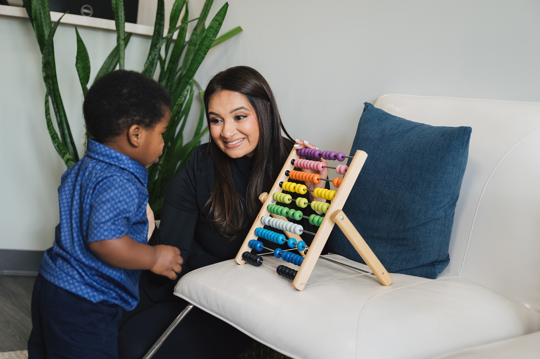 Woman smiling and showing a colorful abacus to a toddler standing nearby.
