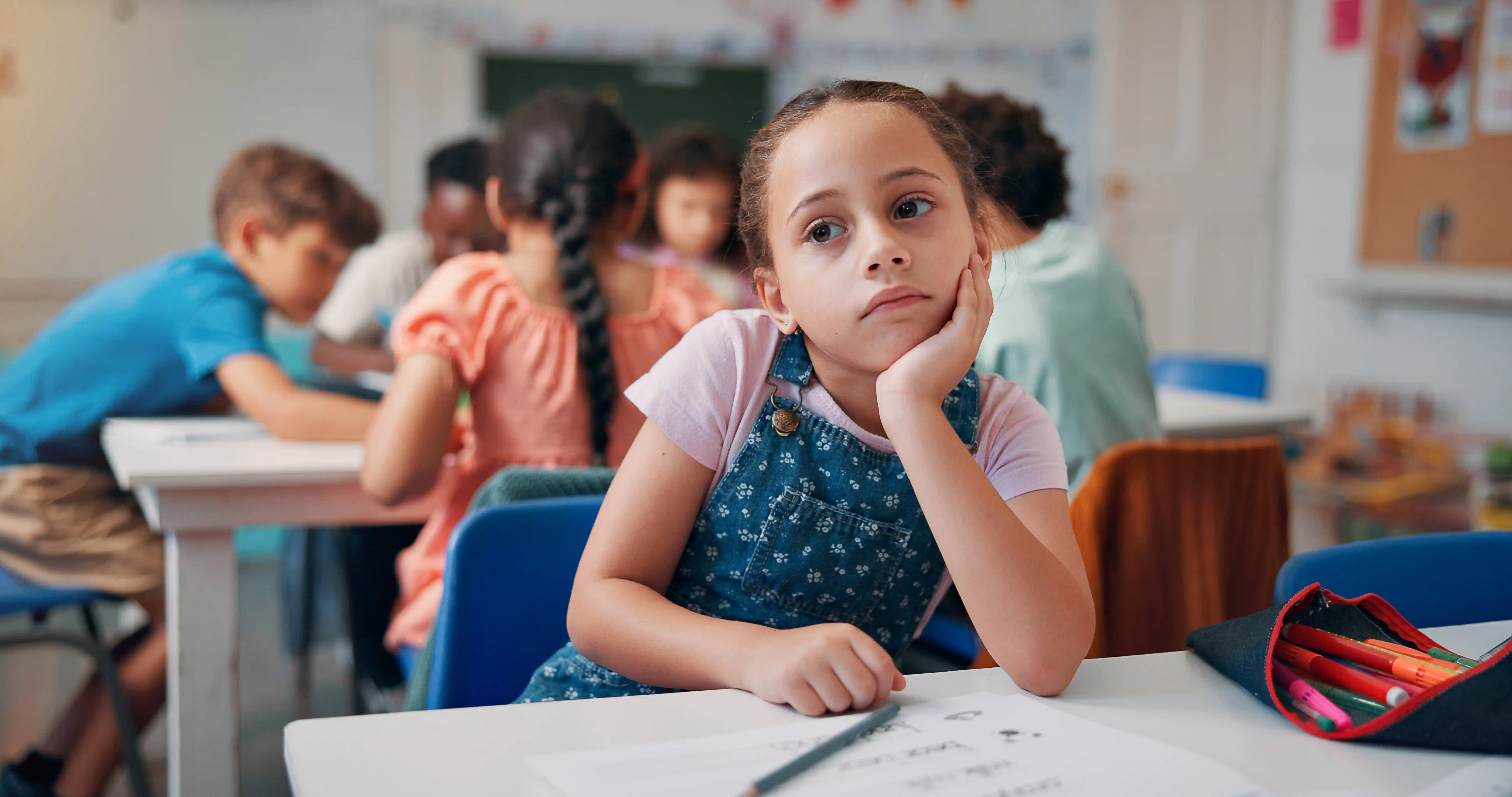 Enfant songeuse à son pupitre pendant que la classe travaille, un motif fréquent d'évaluation TDAH