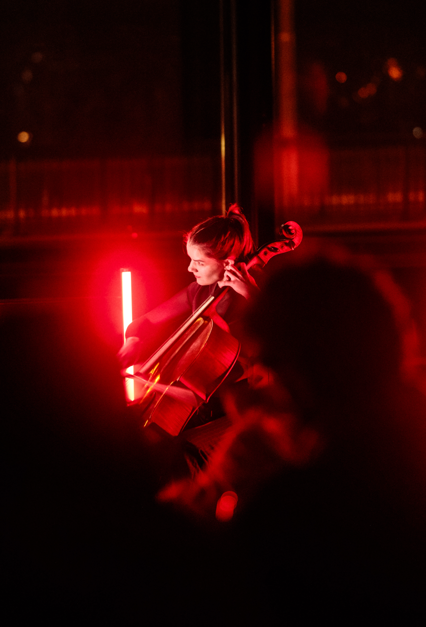 Cellist Katarina Leskovar in concert, smiling. The stage is lit red.