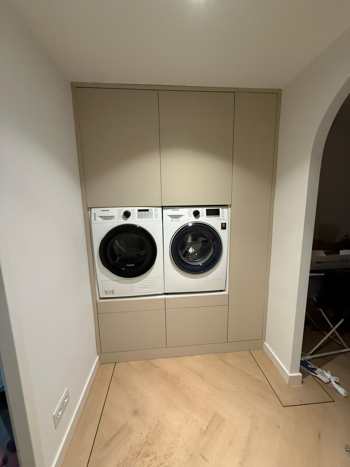 Wasmachine en droger naast elkaar ingebouwd in een beige kast met een lichte houten vloer.