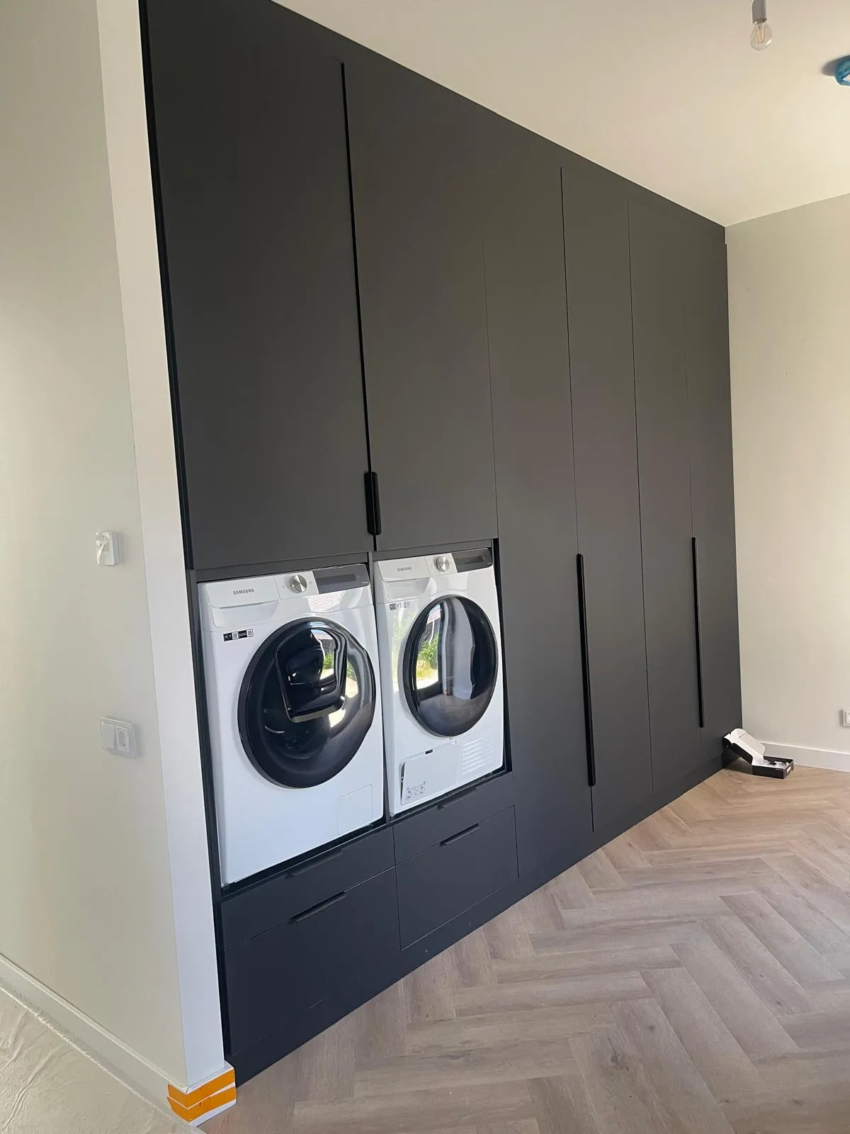 Moderne wasruimte met ingebouwde zwarte kasten en een wit Samsung wasmachine en droger naast elkaar.