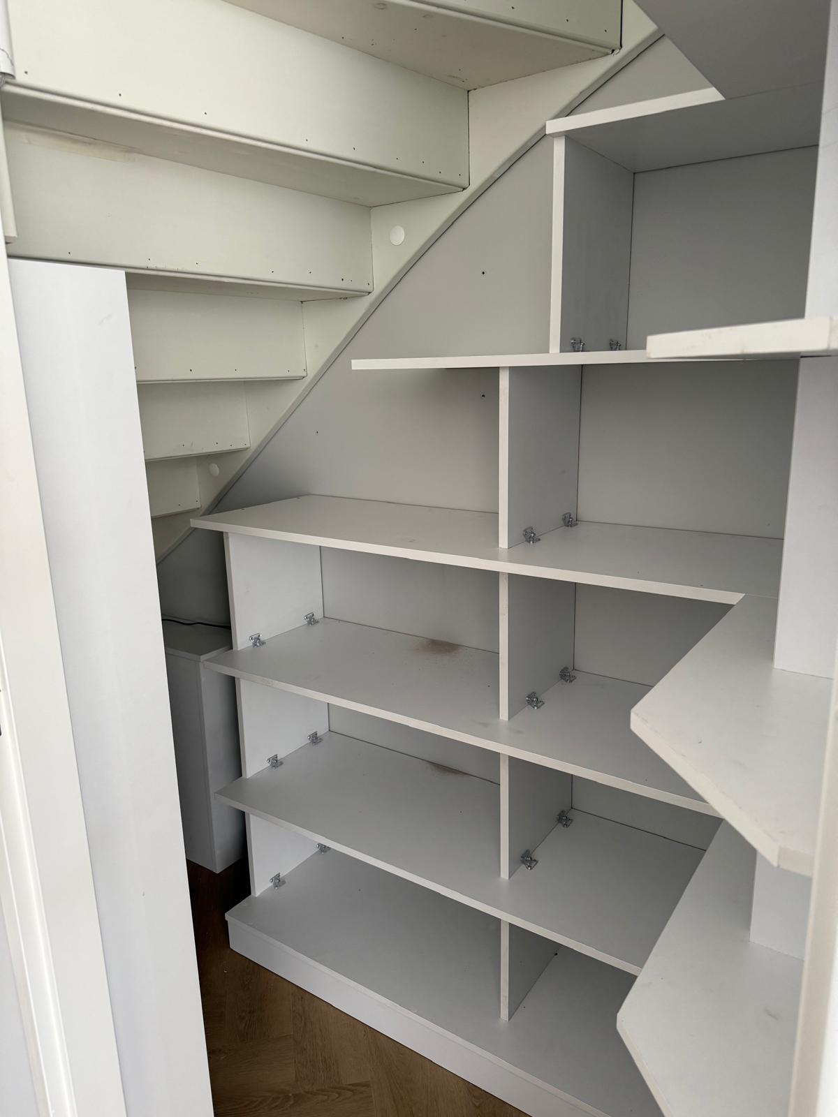 Lege witte planken en kasten onder een wenteltrap in een kleine opslagruimte.