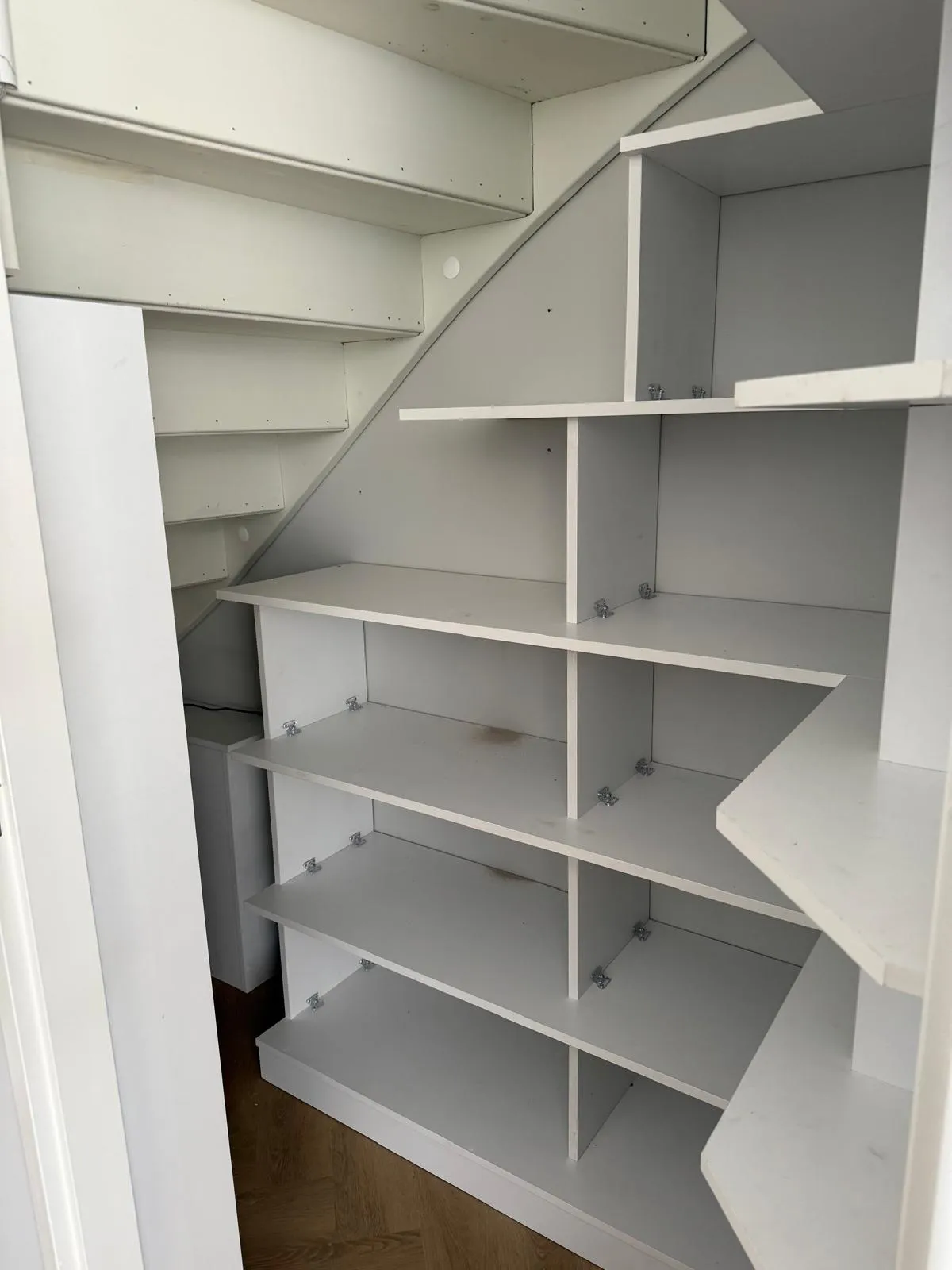 Lege witte planken en kasten onder een wenteltrap in een kleine opslagruimte.