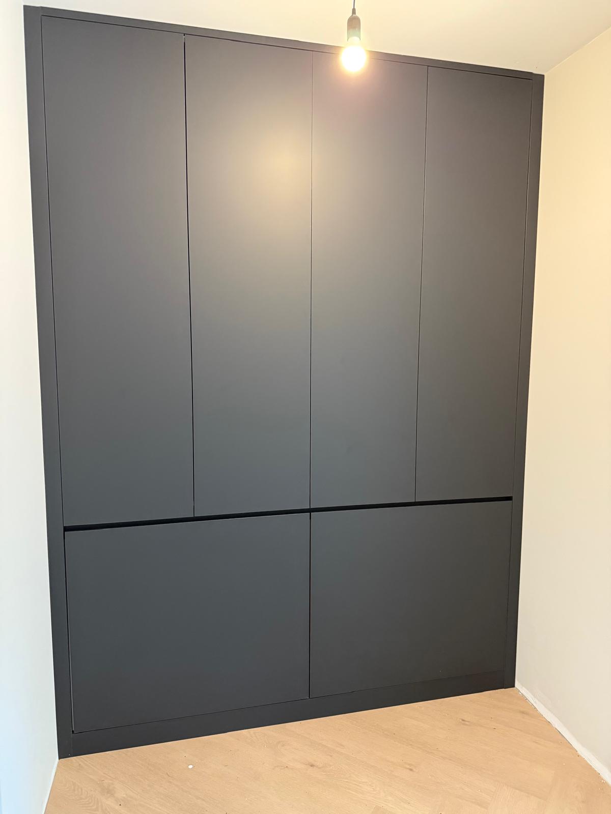 Zwart ingebouwd kastmeubel met zes deuren in een kamer met houten vloer en witte muren.