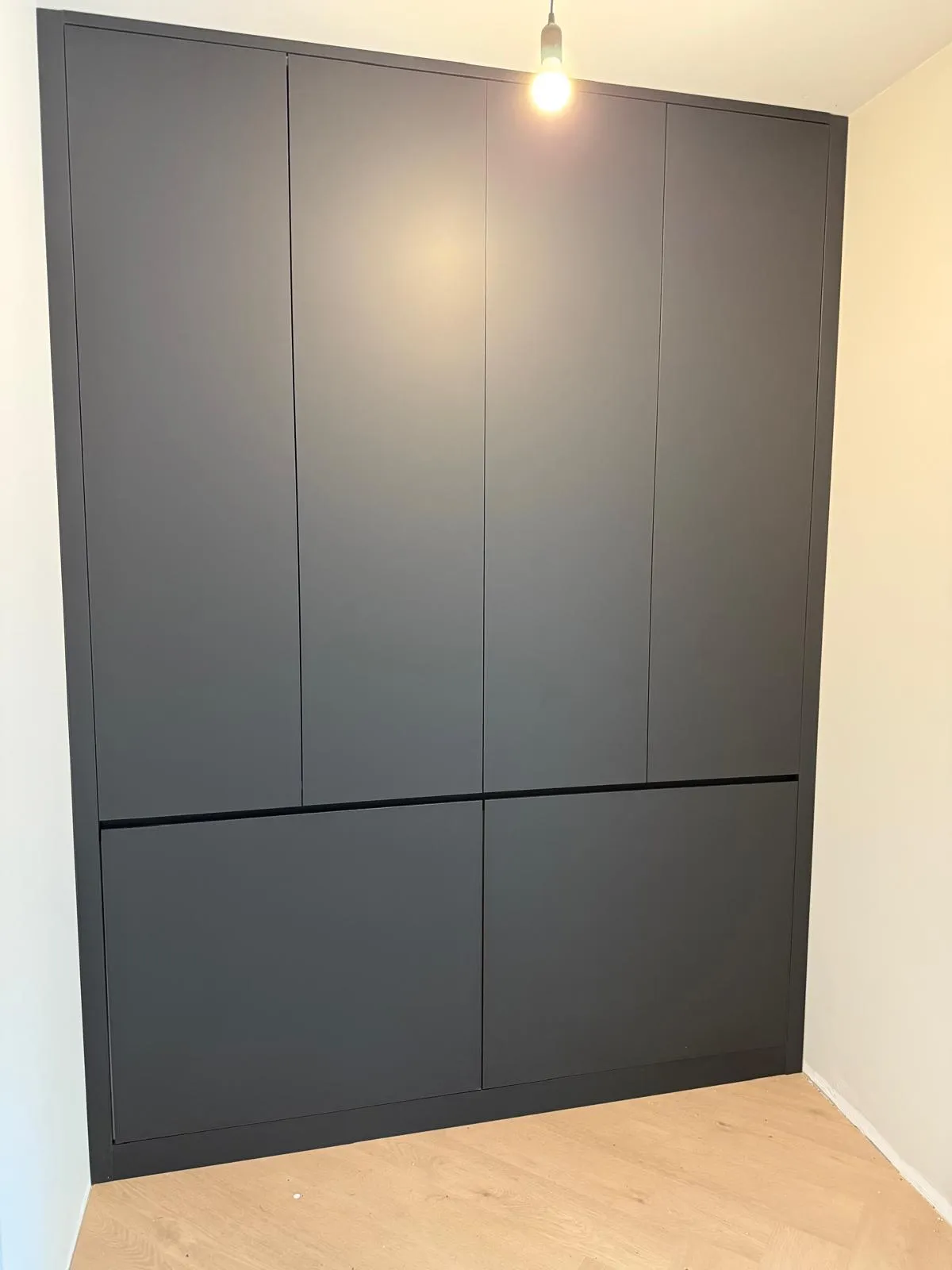 Zwart ingebouwd kastmeubel met zes deuren in een kamer met houten vloer en witte muren.