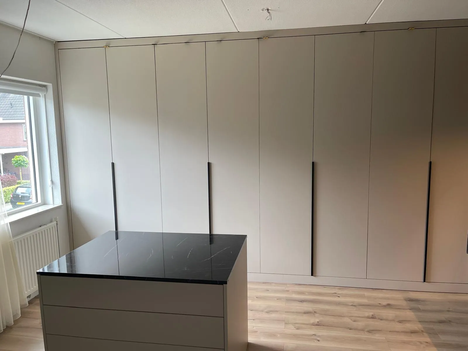 Moderne slaapkamer met grote grijze ingebouwde kasten en een centrale kledingkast met zwart marmeren blad.