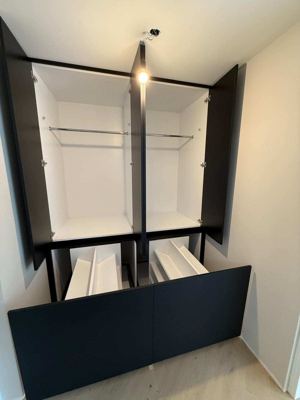 Lege zwarte en witte kast met open deuren en lades, ingebouwd in een lichte kamer.