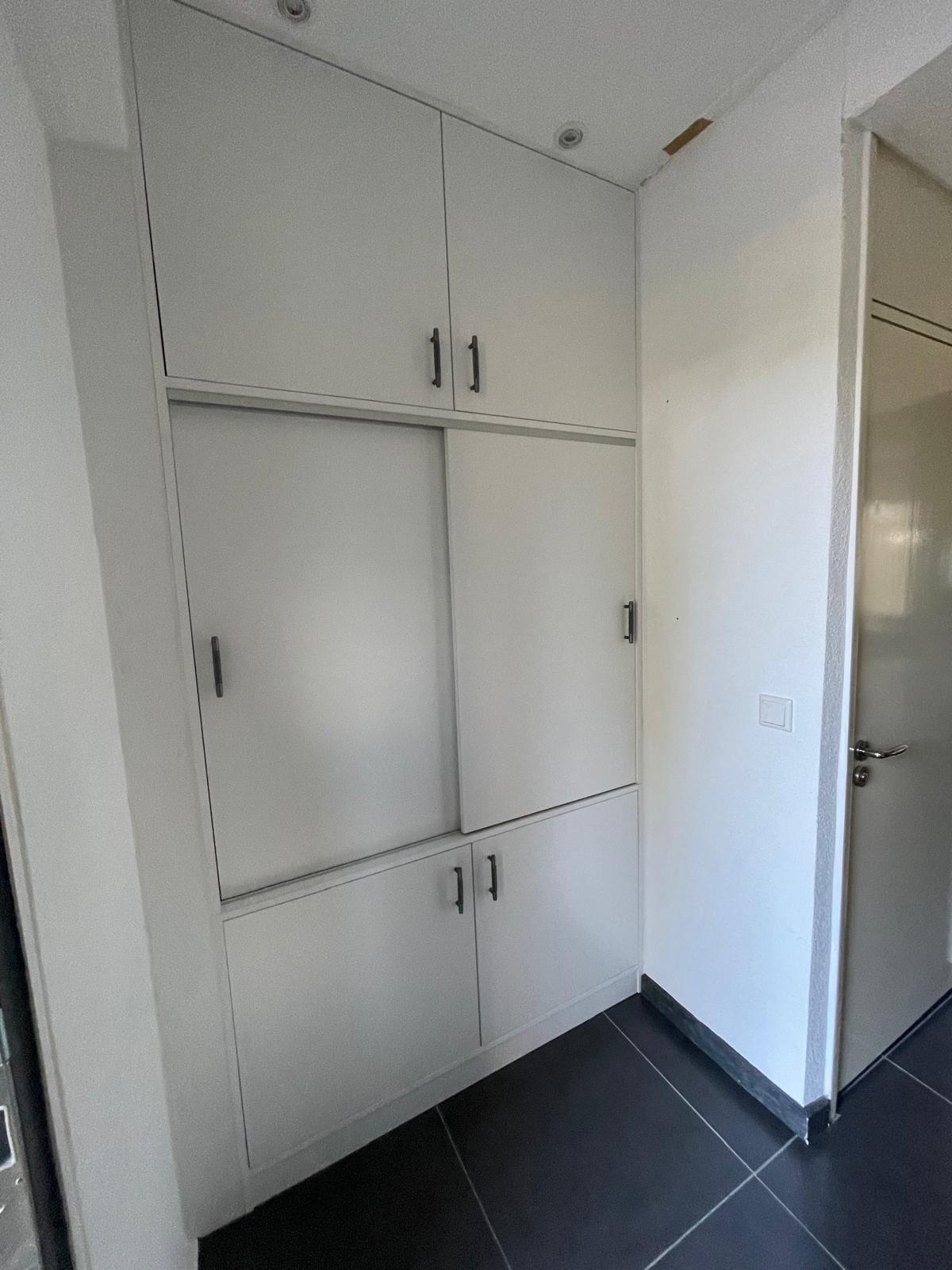 Witte ingebouwde kast met meerdere deurtjes en zwarte grepen in een gang met zwart-witte vloer.
