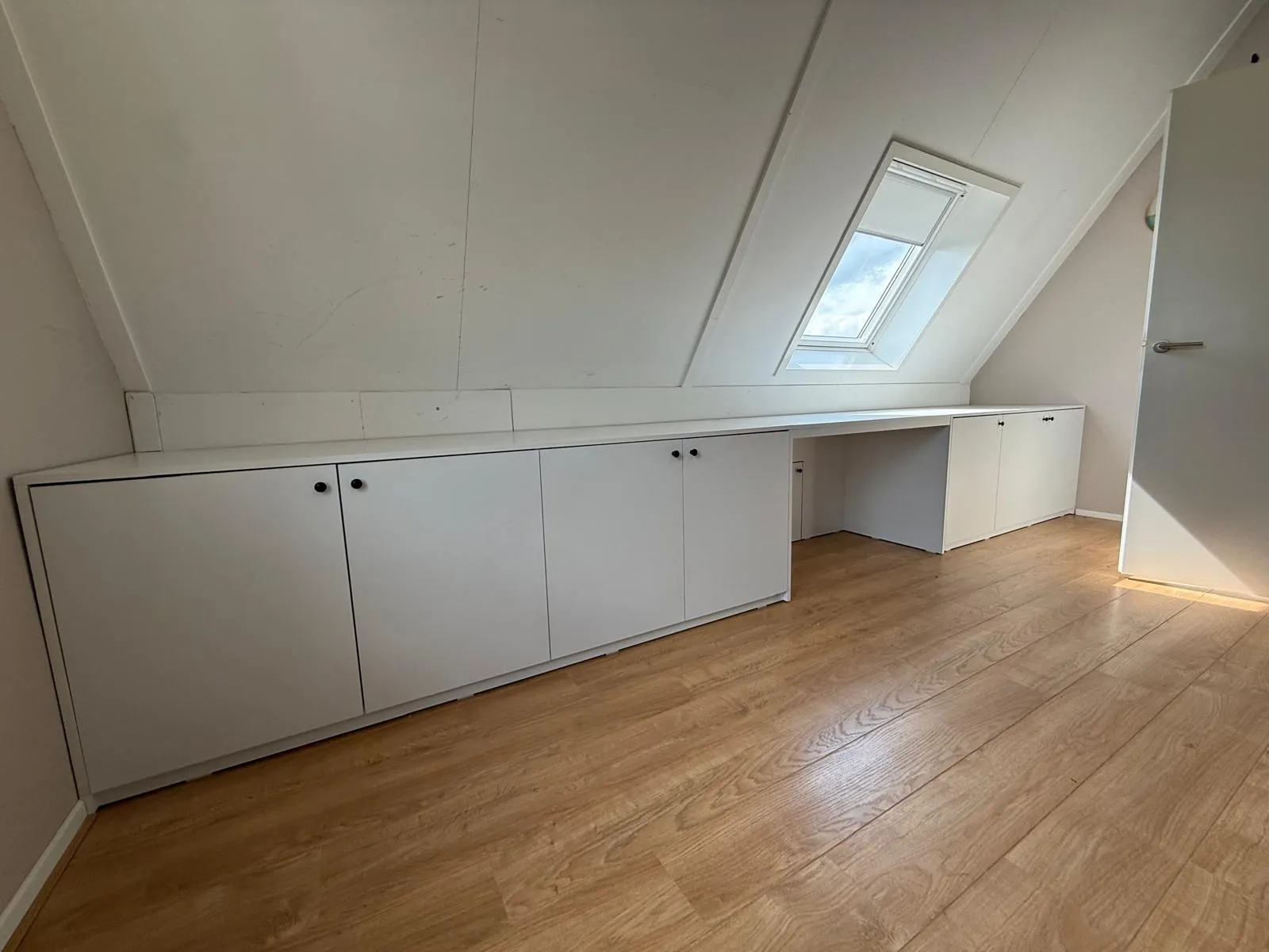 Witte lage opbergkasten onder een schuine wand met een dakraam en een licht houten vloer.