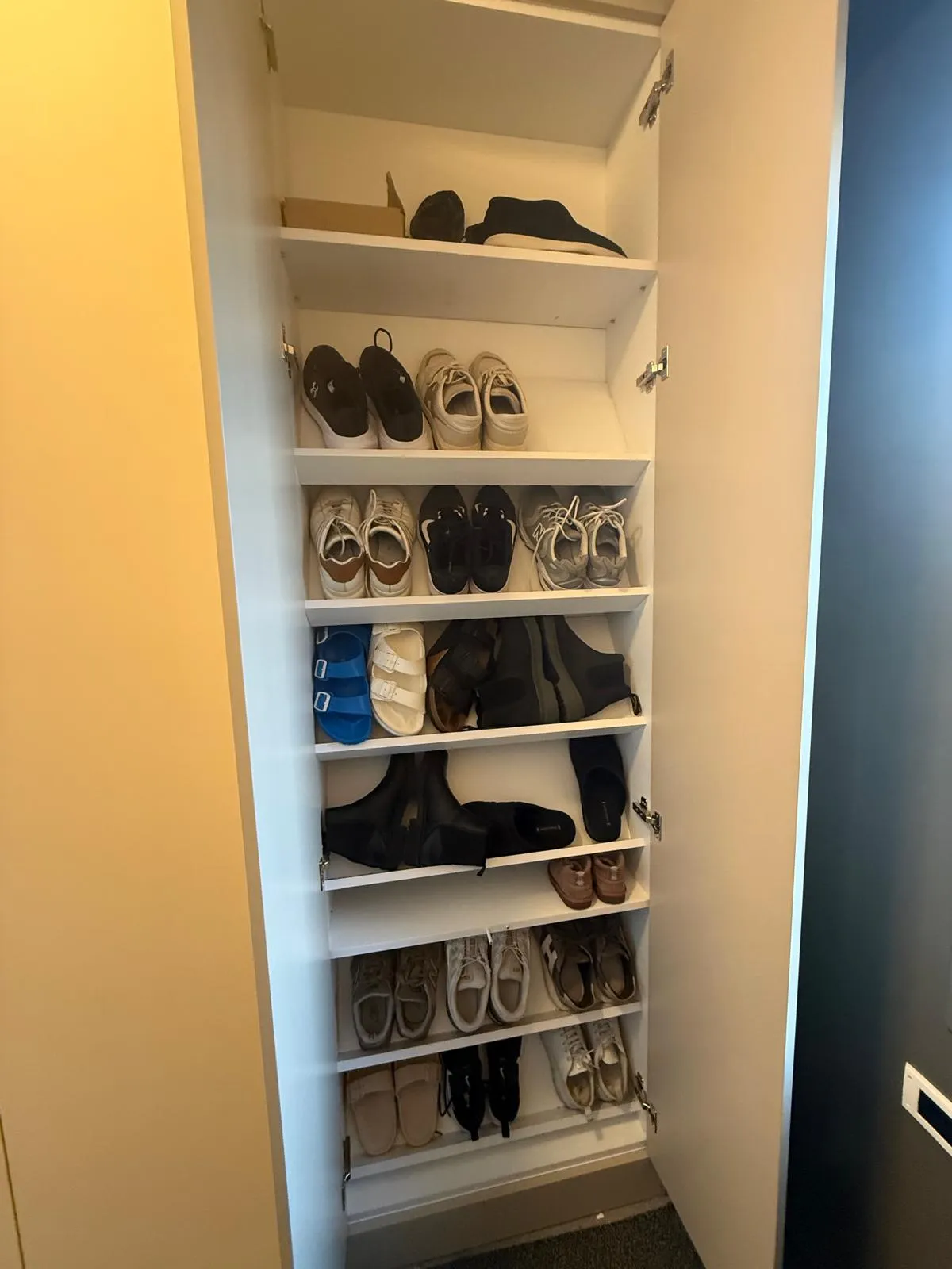 Witte kast met open deur gevuld met verschillende paar schoenen en sandalen op meerdere planken.