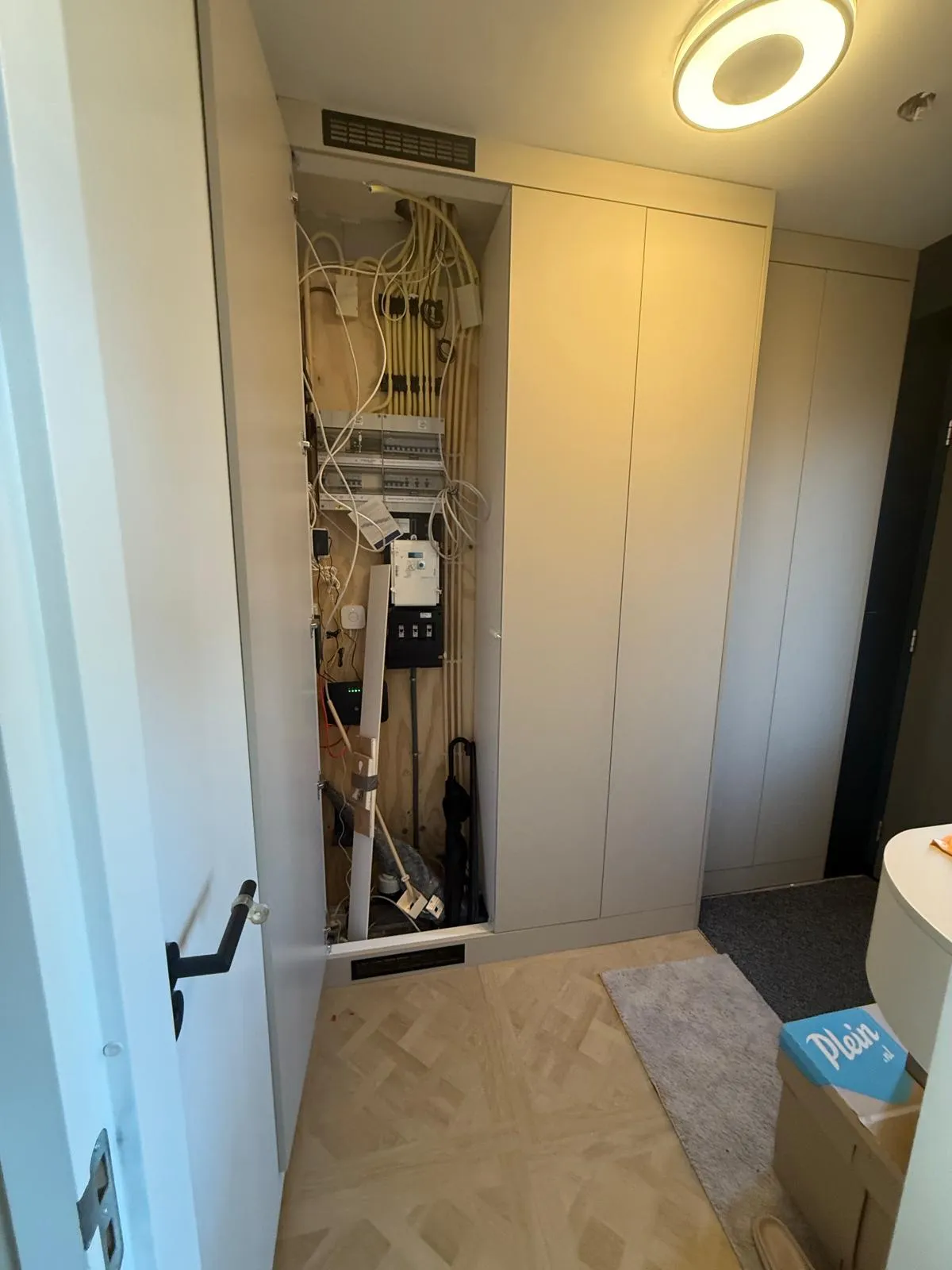 Open closet door showing a panel with electrical wiring and circuit breakers inside a modern home hallway.