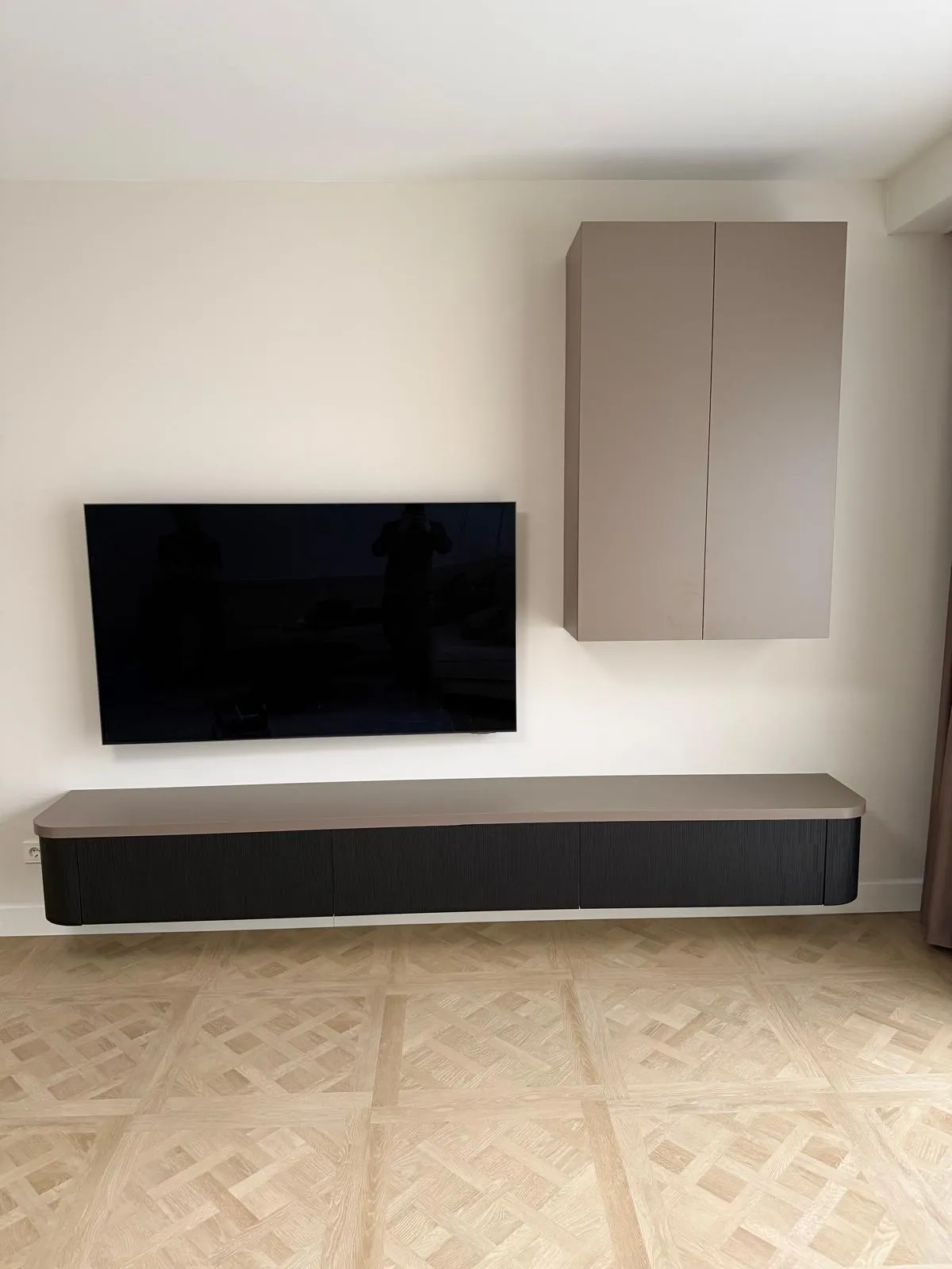 Moderne woonkamerwand met een zwarte muurbeugeltelevisie, een zwevend houten tv-meubel en een bovenkastje aan de muur.