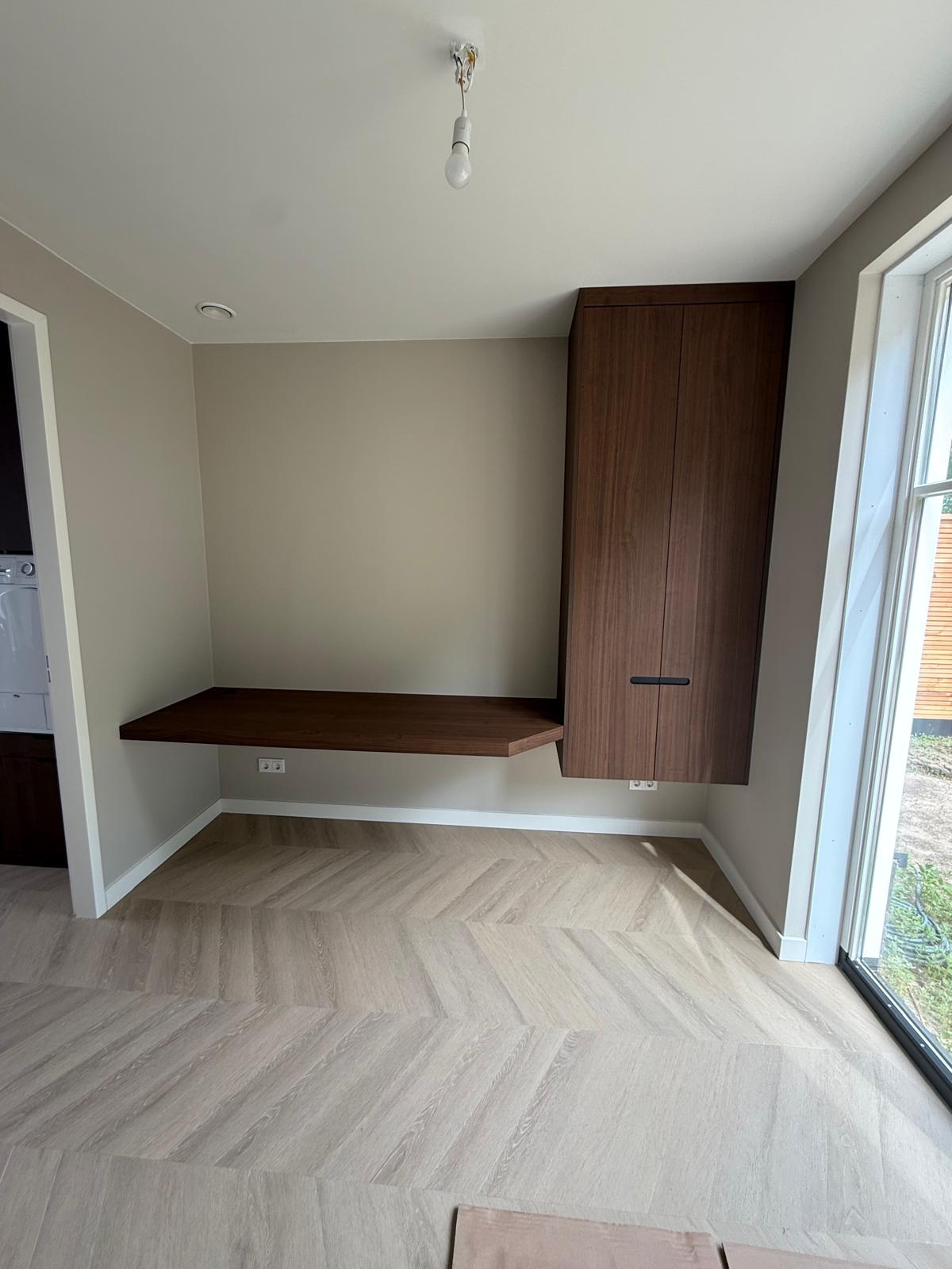 Lege kamerhoek met zwevend houten bureau en hoge houten kast naast raam.