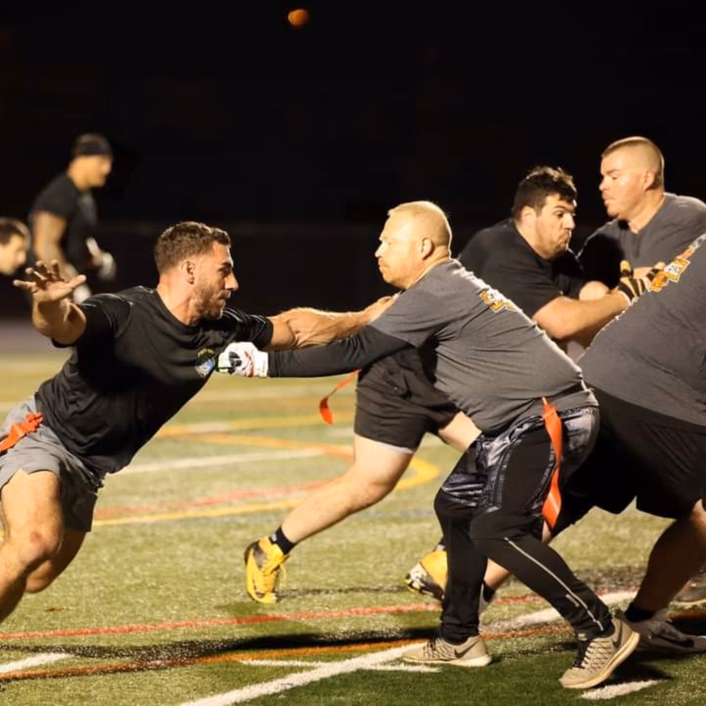 A group of men playing football on a grassy field, wearing sportswear and footwear, engaged in a competitive game outdoors.