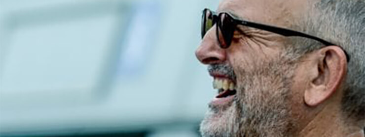 Side profile of a smiling middle-aged man with gray hair, beard, and sunglasses.
