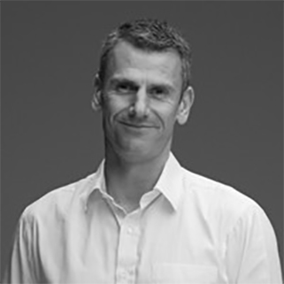 Black and white portrait of a man wearing a white button-up shirt smiling slightly against a plain dark background.