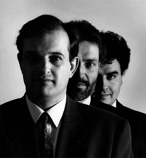 Black and white portrait of three men in suits standing closely in a staggered line, with serious expressions.