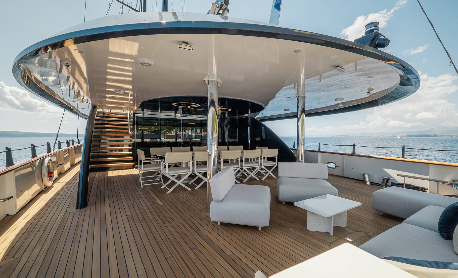 Spacious teak yacht deck with shaded lounge area, dining table, and panoramic ocean views.