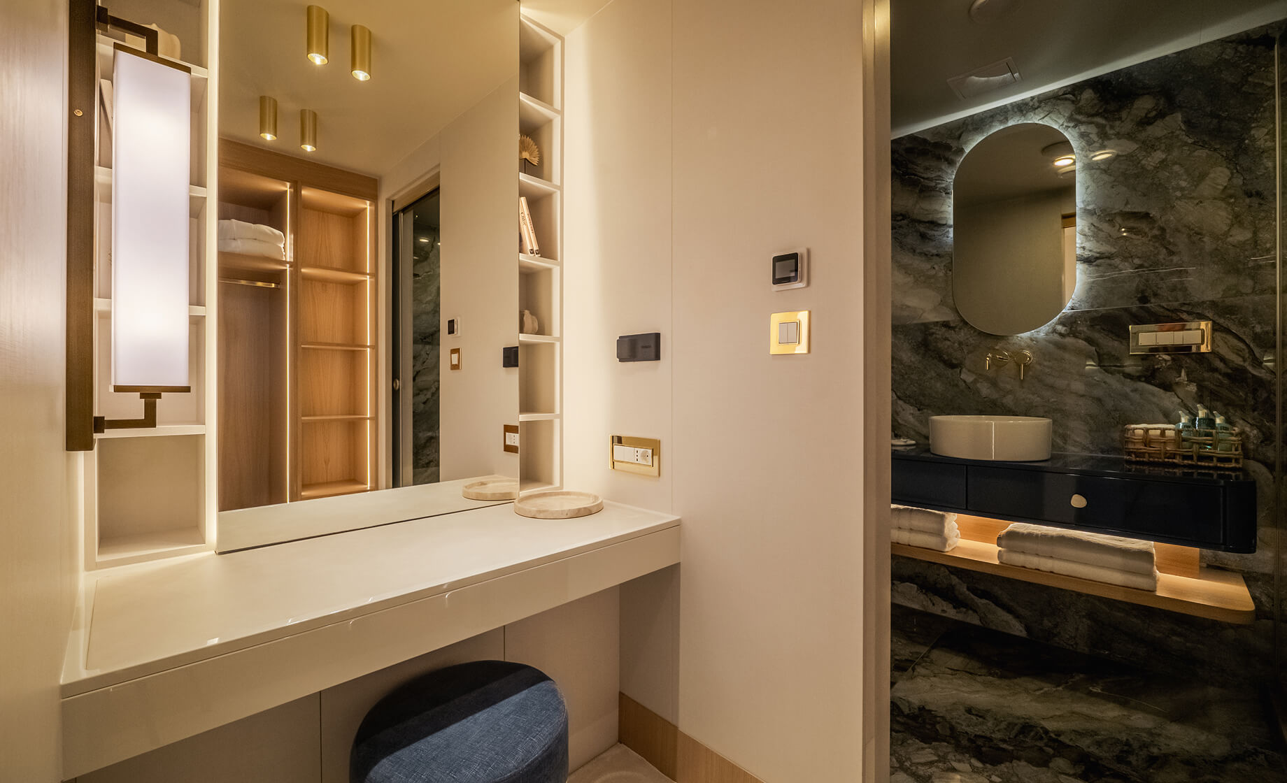 Elegant yacht bathroom and vanity area with illuminated mirror, marble wall finishes, vessel sink, built-in shelving, and warm ambient lighting.