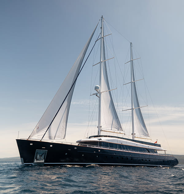 Luxury black sailing yacht with two tall masts and white sails cruising on calm blue water under a clear sky.