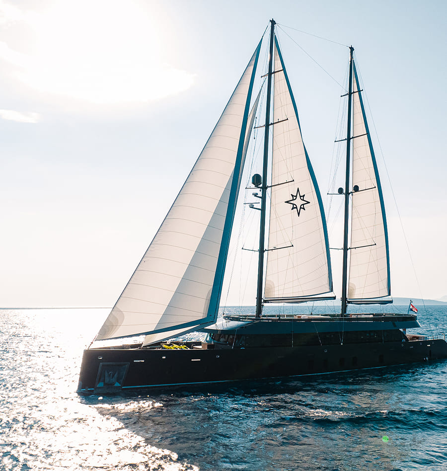 Luxury black sailing yacht with two tall masts and white sails featuring a star emblem, cruising on sunlit open water.