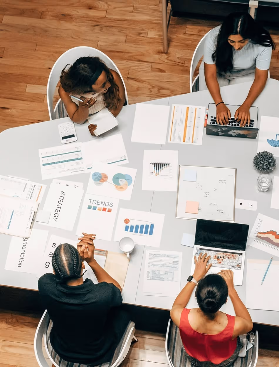 Four people having a business meeting around a table with laptops, charts, and documents.