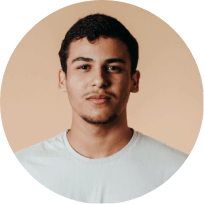 Portrait of a young man with short curly hair wearing a white shirt against a beige background.