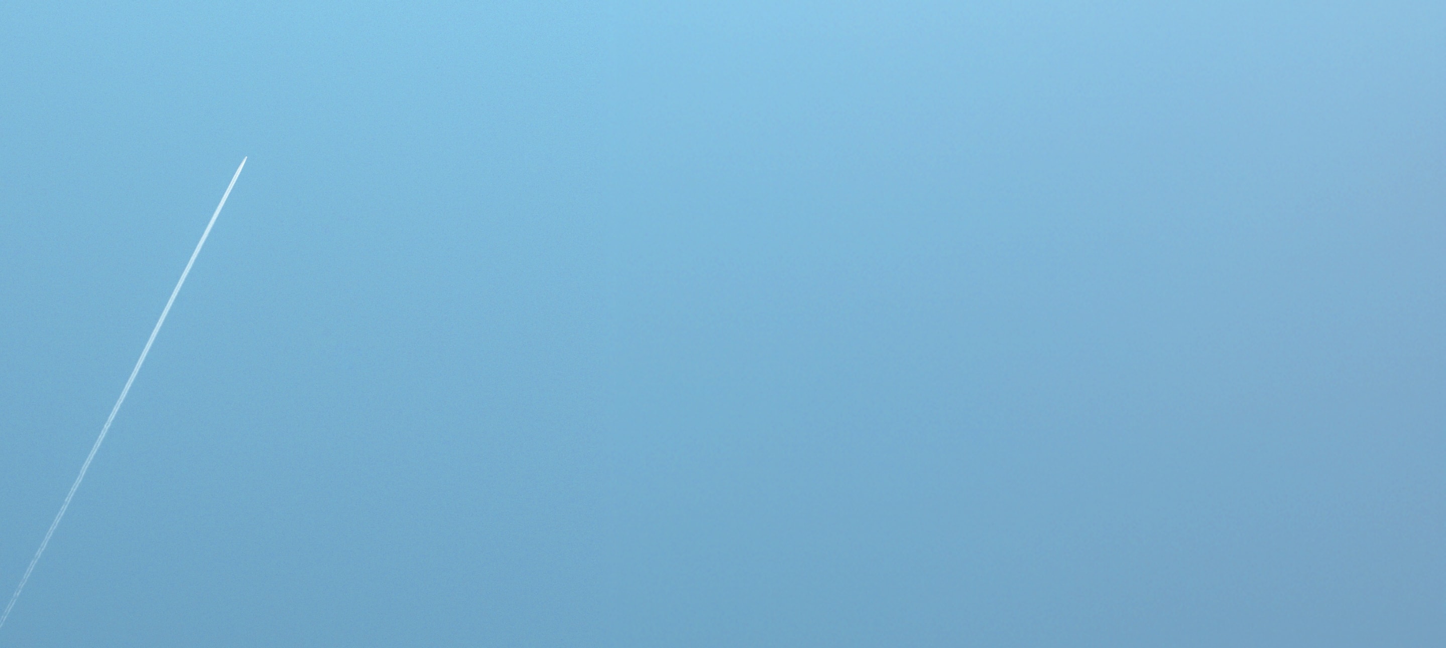 Clear blue sky with a single white vapor trail from a high-flying airplane.