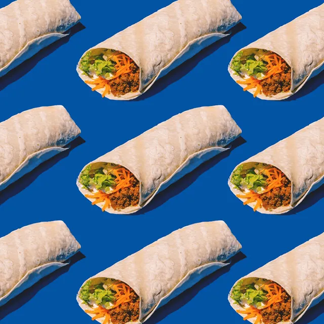 A pattern of burritos on a blue background, each filled with lettuce, shredded carrots, and other colorful ingredients, creating a vibrant and appetizing display.